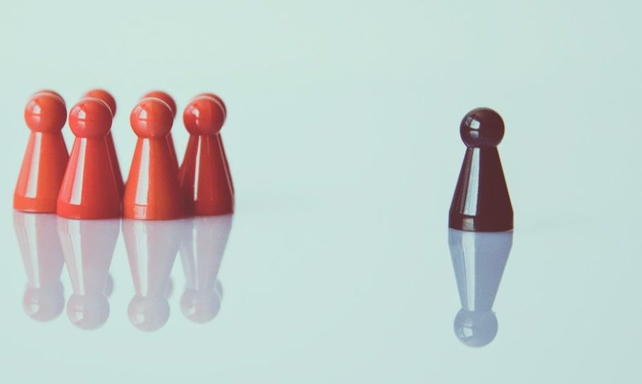 Perfekter Mitarbeiter gefunden Fünf rote Spielfiguren stehen links, eine schwarze Figur steht allein rechts als Symbol für den einen perfekten Mitarbeiter.